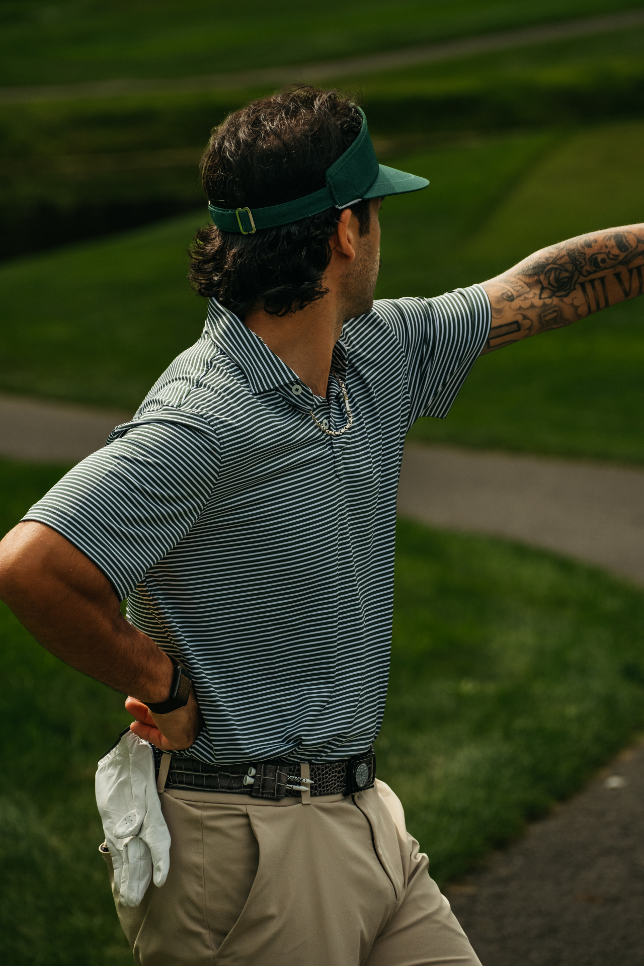Dartee golfer in a green visor and striped polo wearing a Dartee ratchet belt against a Lowcountry tree line