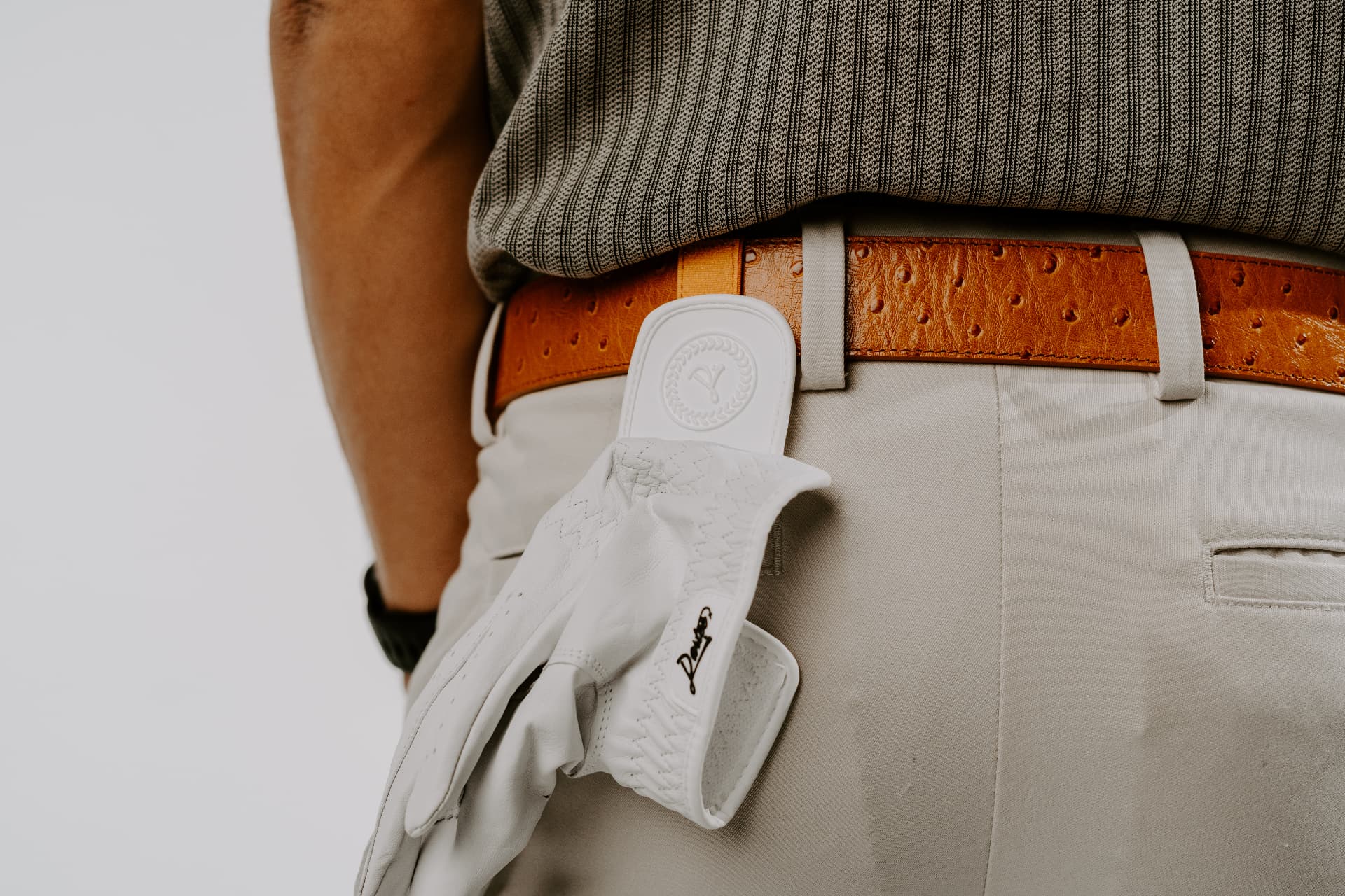 Close-up of a golfer wearing a striped polo and a tan Dartee ostrich leather belt with a white golf glove