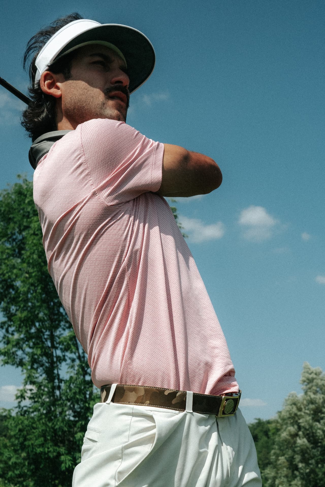 Golfer mid-swing on the course in a pink polo wearing a Dartee camo ratchet belt with the magnetic buckle